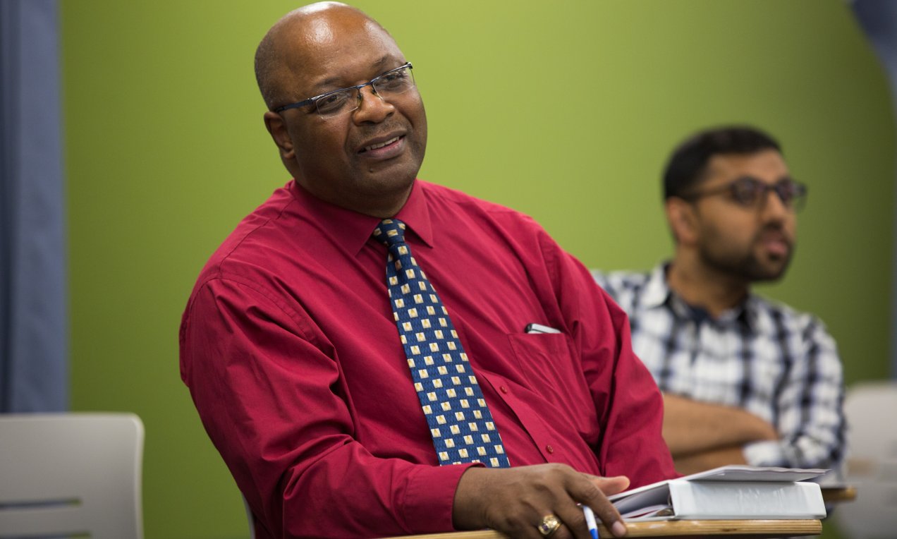 A man looking listening with another man behind him.